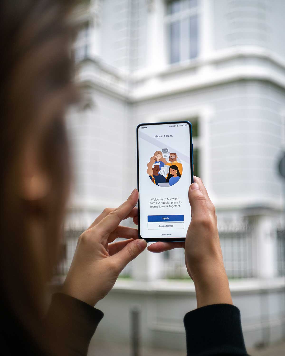 A person holds a mobile phone showing the Teams logo