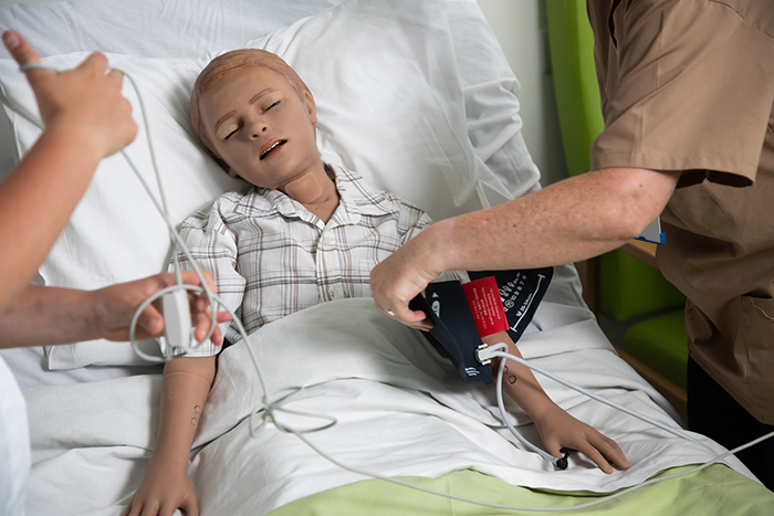 A medical mannequin of a child in a hospital bed being used by medical students. 
