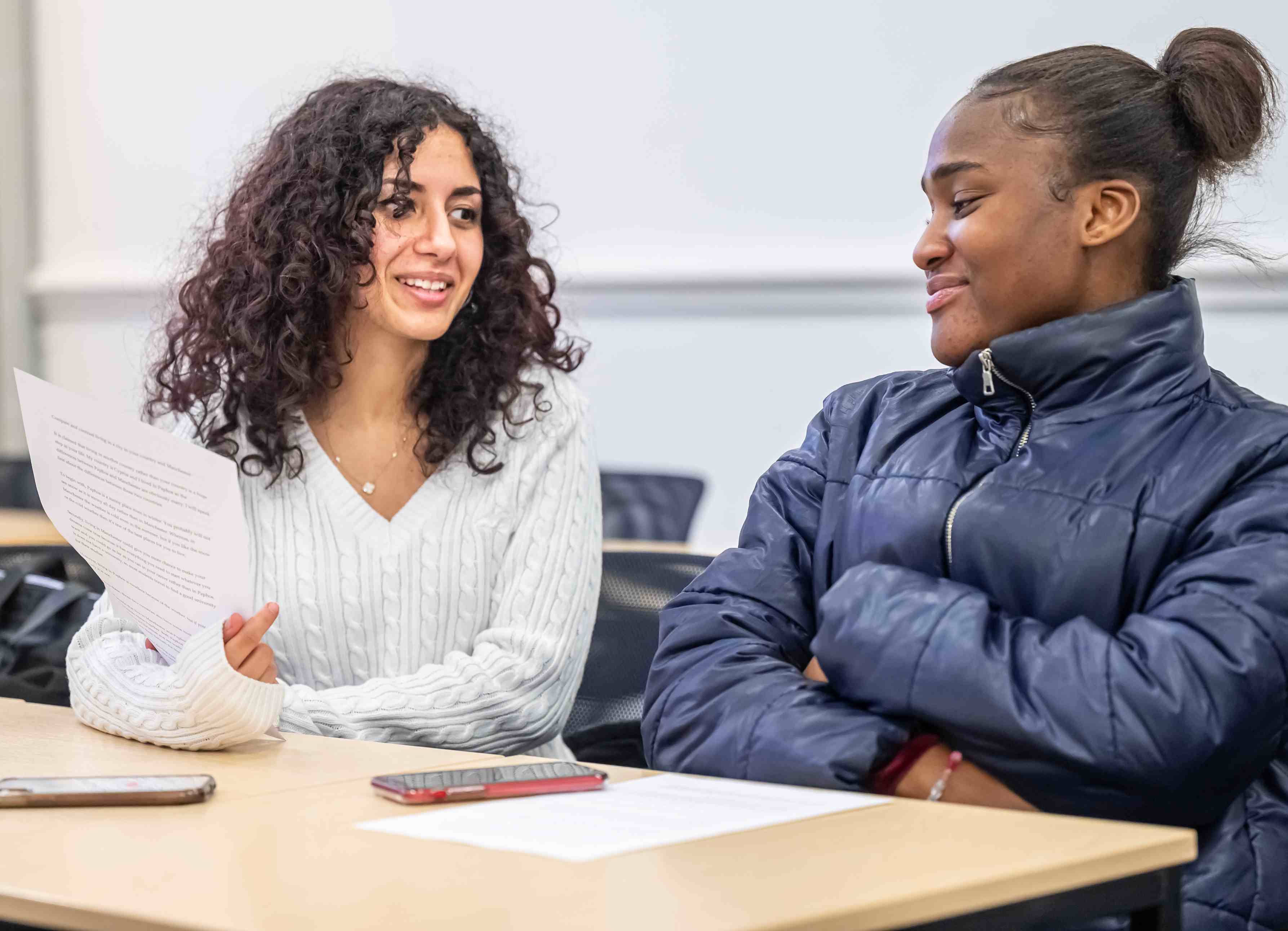 Two international foundation year students in a classroom chatting look at a piece of paper