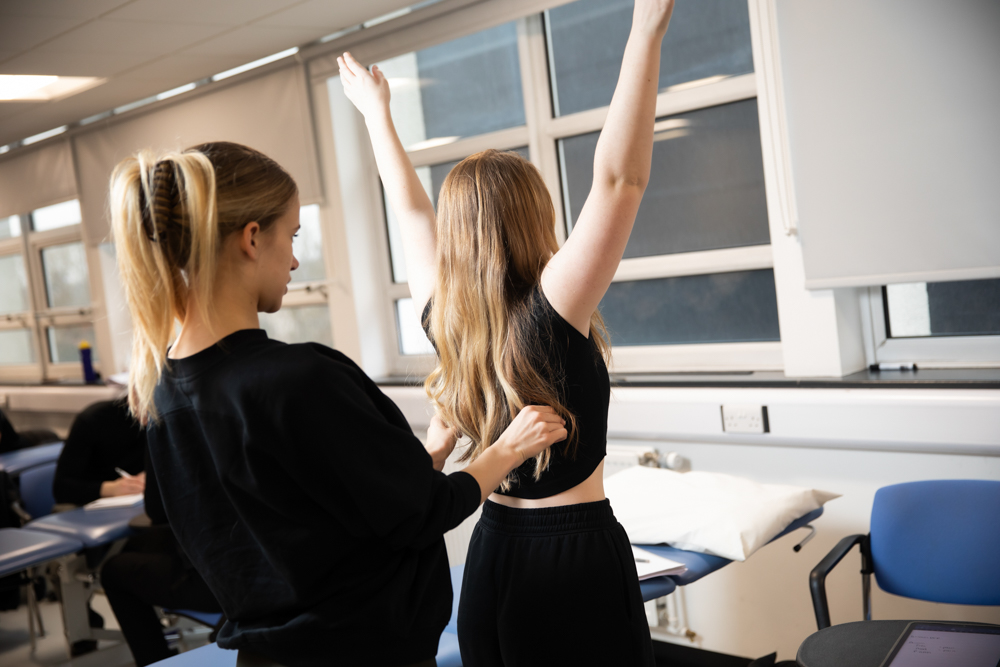 Female student standing behind another conducting a musculoskeletal assessments