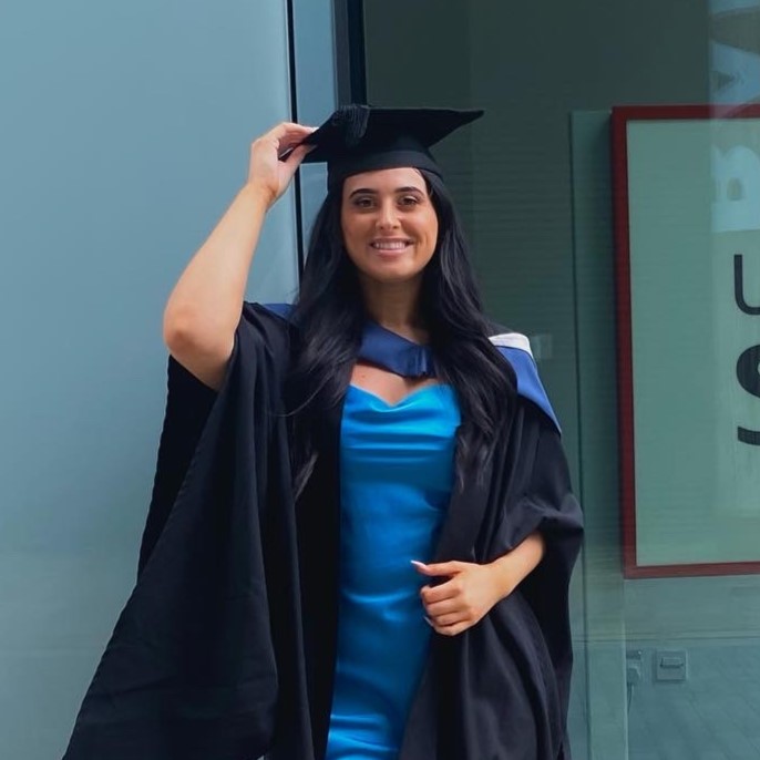 Bethany wearing a blue dress and a graduation gown and cap.