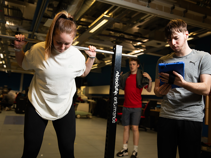 In our Human Performance Laboratory, a student undergoes a strength and lifting test, observed by two other students. One student records the results.