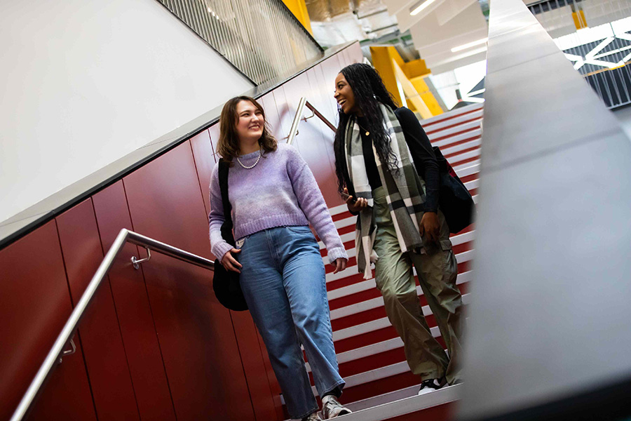 Two students smiling and walking down the stairway together in Salford's SEE building