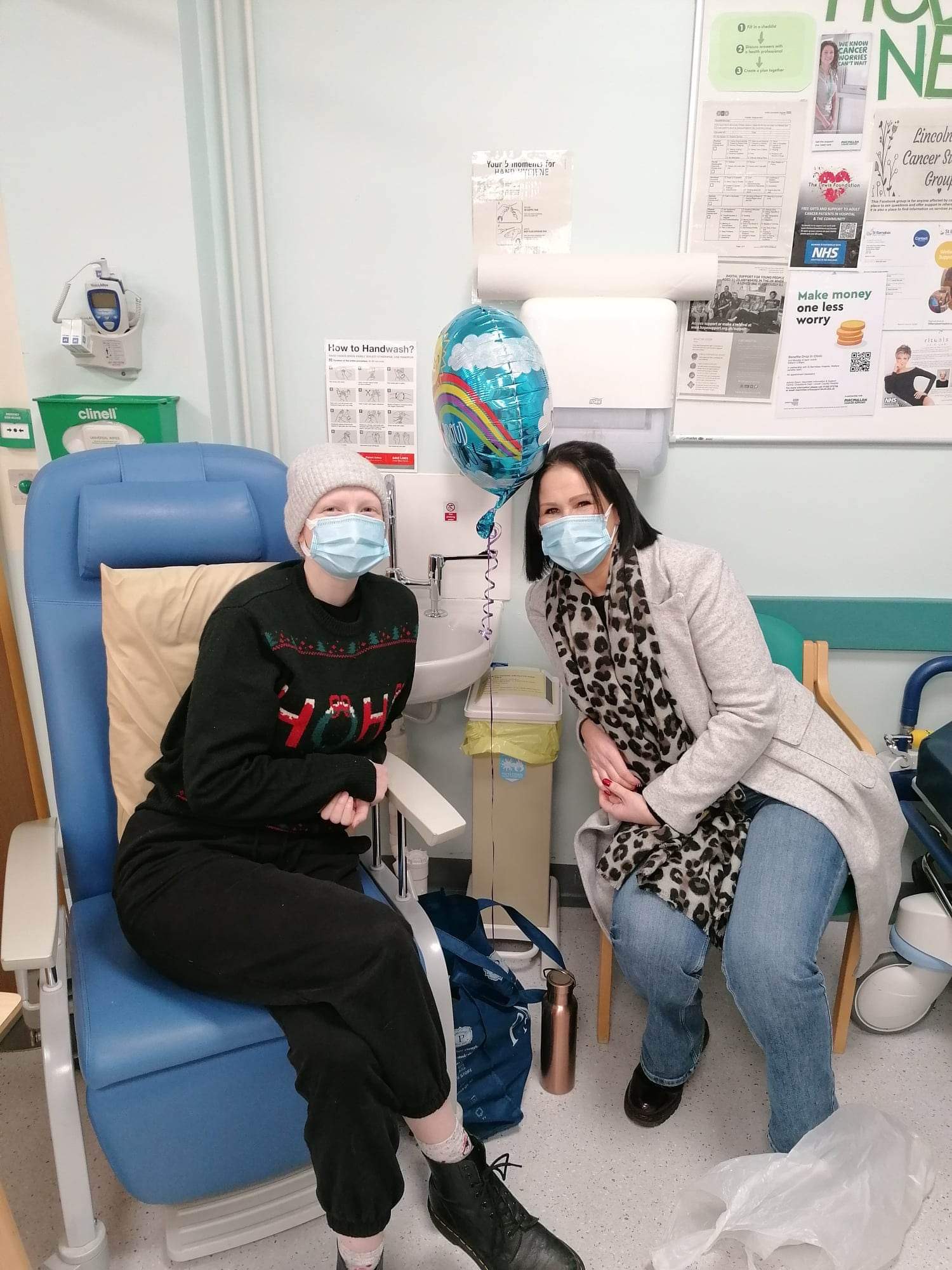 A girl in hospital with a face mask on and her mother sat alongside her also wearing a face mask