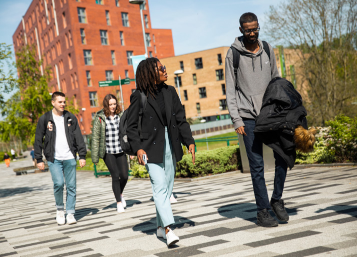 Four students walking through the Peel Park campus, University of Salford