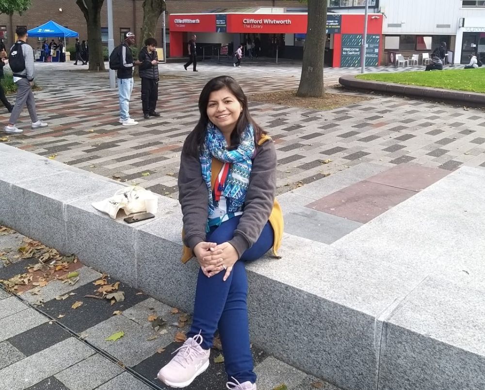 A female student sat crossed legged on our Peel Park campus in front of the Clifford Whitworth Library