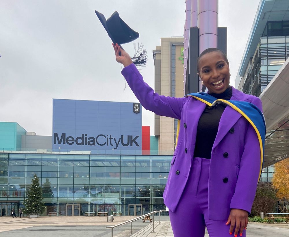 A female student in a purple suit and graduation robes in the middle of MediaCity