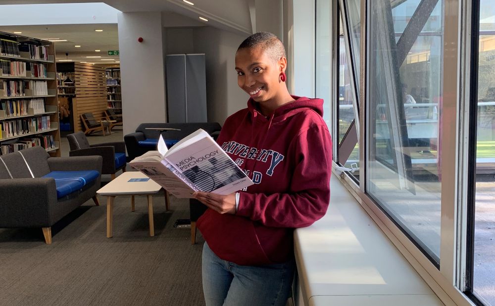 A female student reading a Media Psychology textbook in a library 