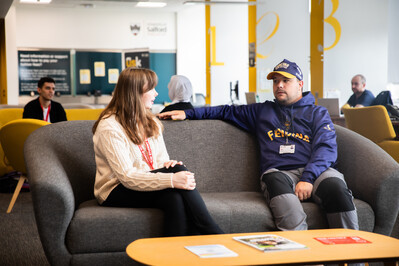 Two students sat talking on a settee 