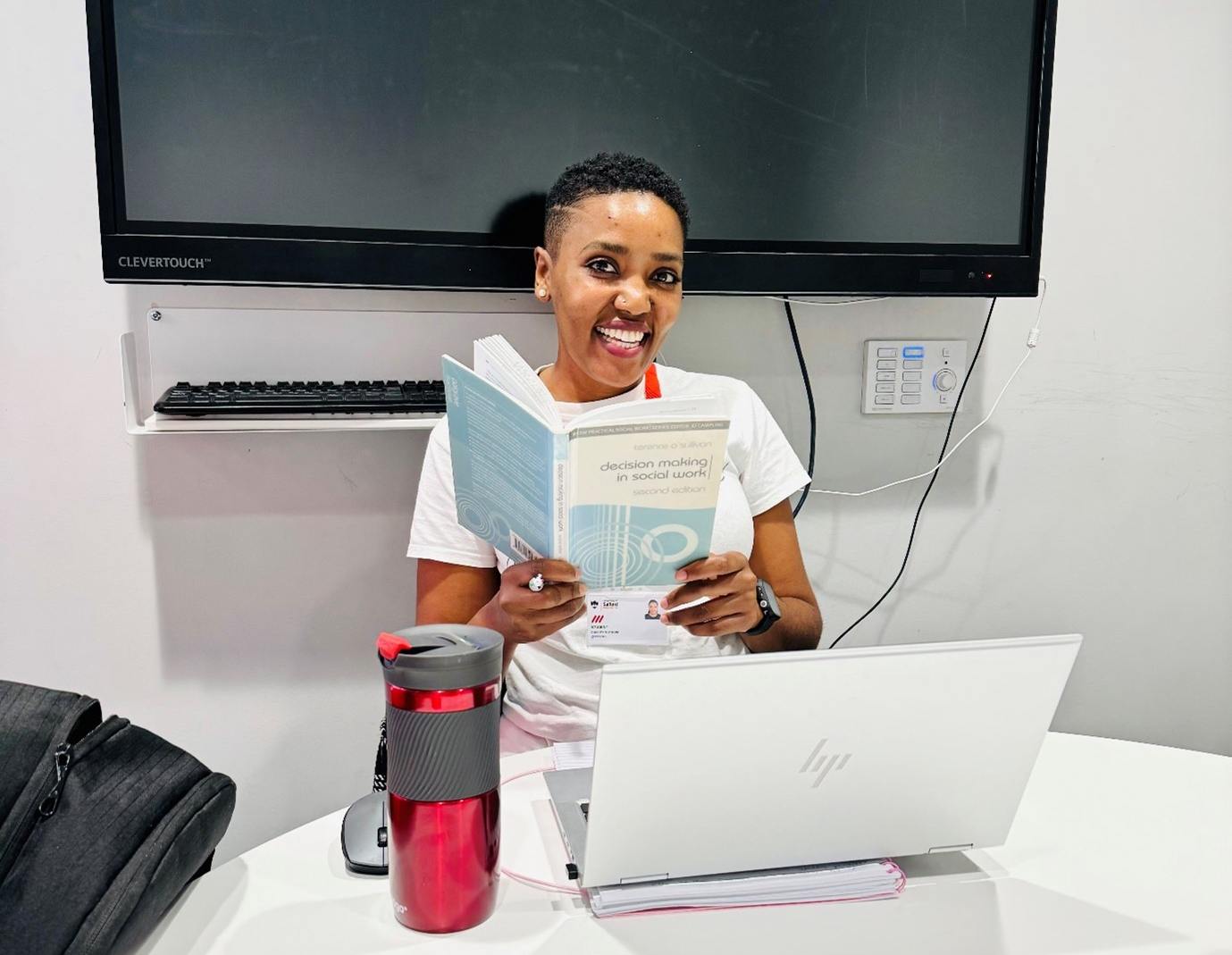 A female student sat in a study room in front of a laptop holding a text book open in front