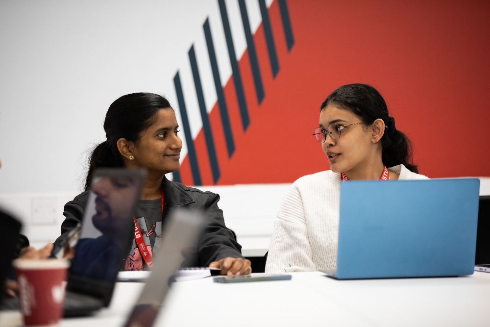 Two students sat chatting behind laptops