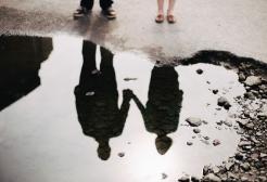 Two people holding hands in the reflection of a puddle