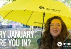 A campaign image for Dry January, showing a smiling woman stood under an umbrella