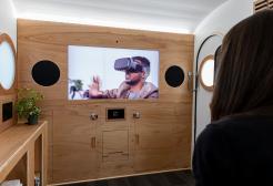 Image shows the interior of the caravan from the future with a big screen and a person watching