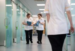 Two podiatry apprentices walking with a folder in their hands talking to each other, and the back of another apprentice.