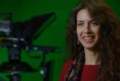 A female student sits in front of green screen and two film cameras 