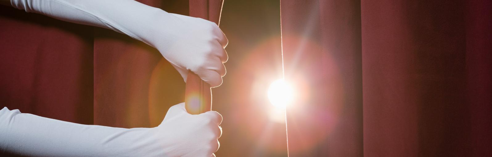 Hands drawing back a curtain