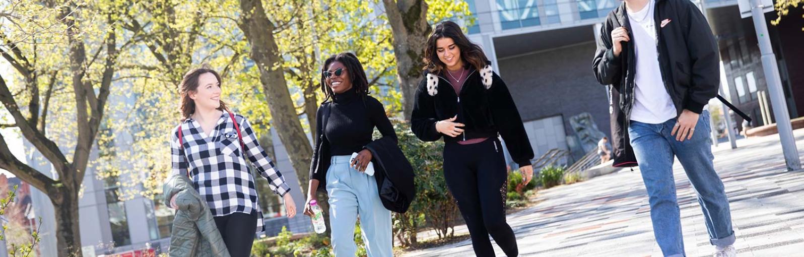 Three female and one male students walking outside through campus