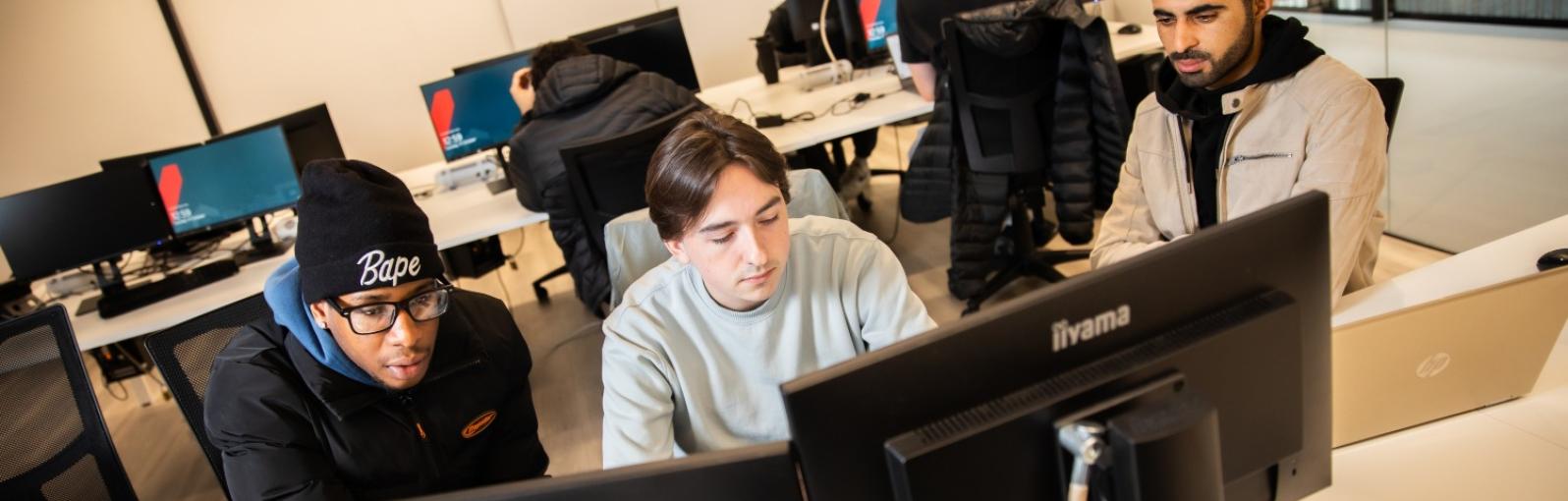 Three male students working together around three computer monitors