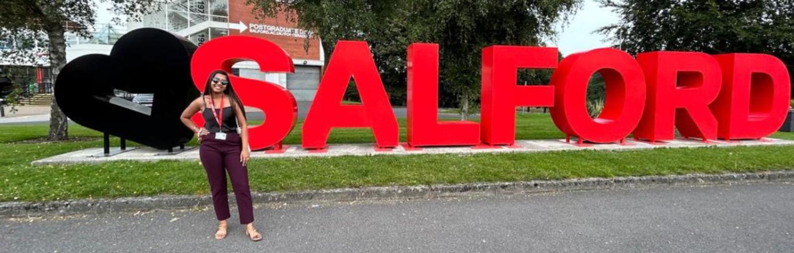 A female student stood in front of the Salford sign