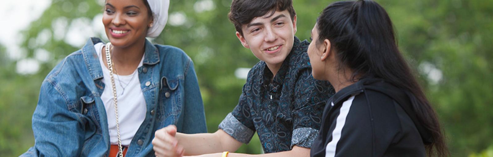 Three students chatting sat outside on grass