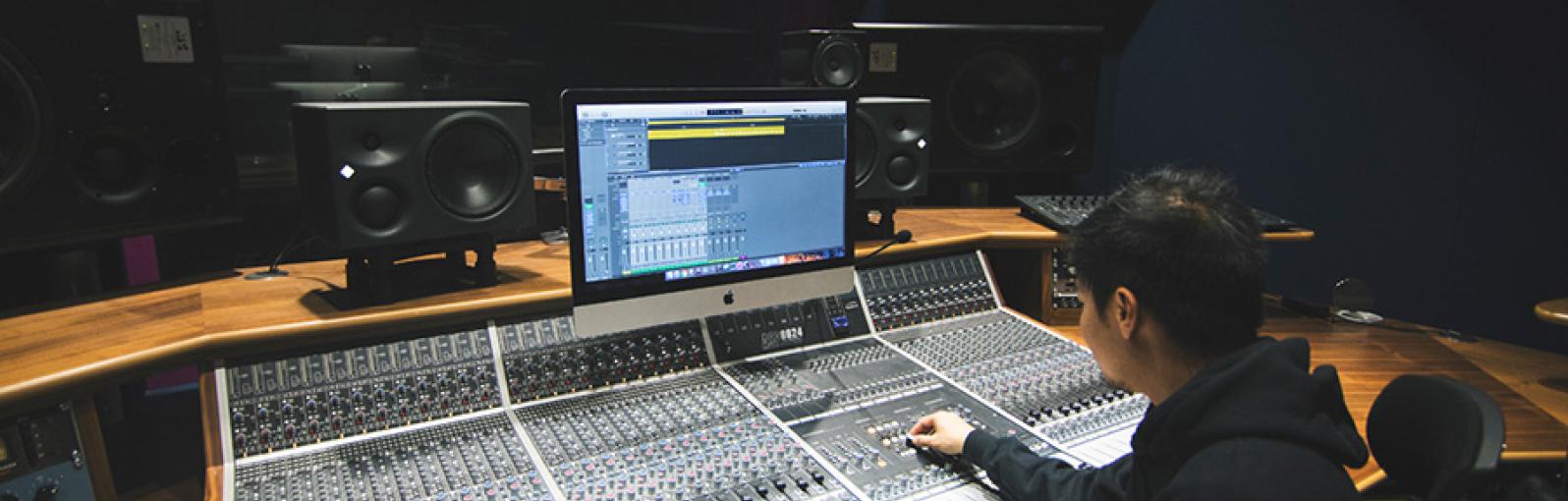 Salford music degree student sitting by high-tech recording equipment in the university’s recording studio facilities.