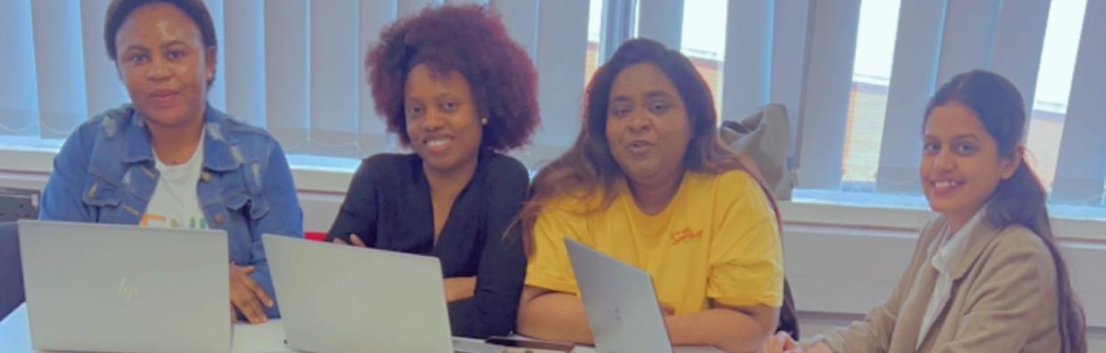 Four students sat around a table studying with their laptops