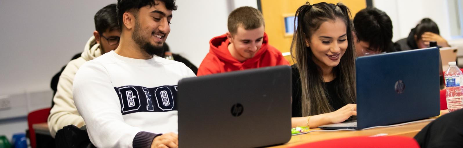 Male and female students in class and on laptops, laughing 