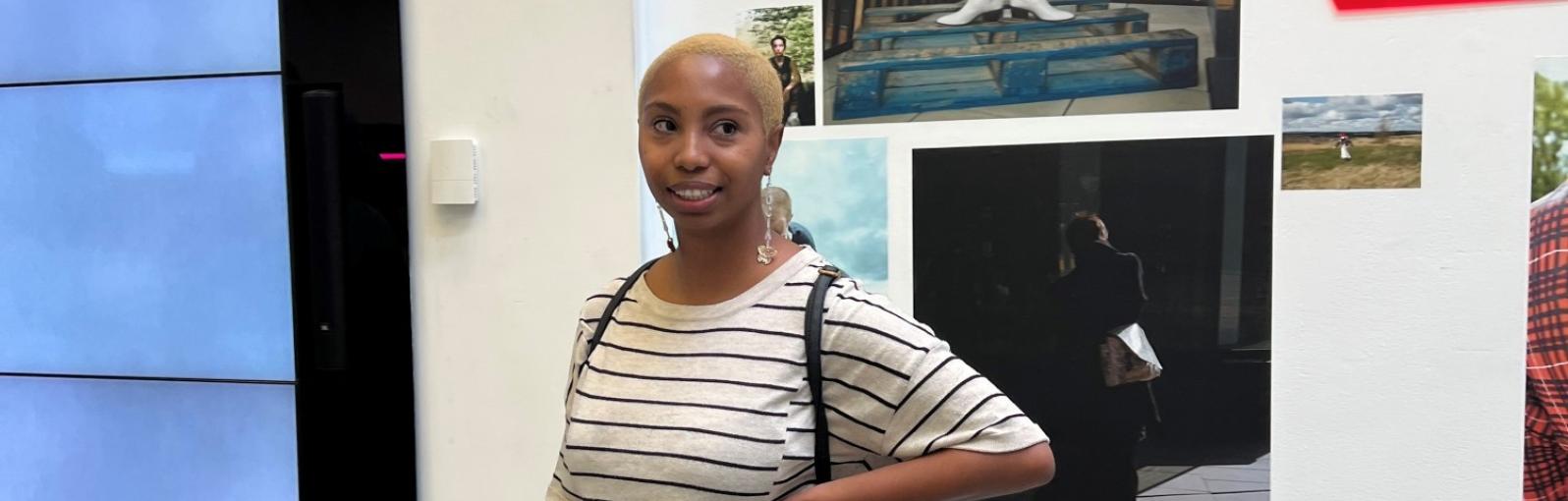 A female student stood in New Adelphi foyer in front of a screen with her hand on her hip looking to the side of the camera