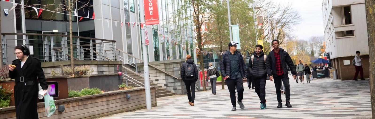 Three male students walking through Peel Park campus next to the New Adelphi