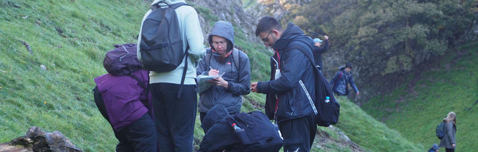 A group of Geography students studying something on the ground on the side of a hill during a field trip