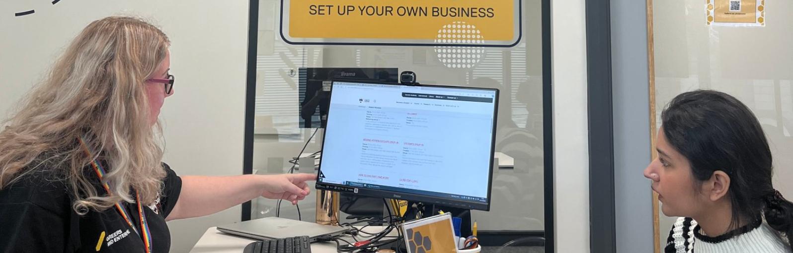 A student sat opposite a help desk looking at a computer 