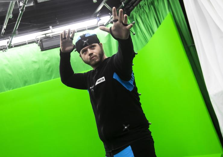 A man is demonstrating motion capture technology in front of a green screen 