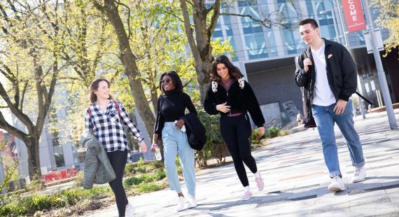 Three female and one male students walking outside through campus