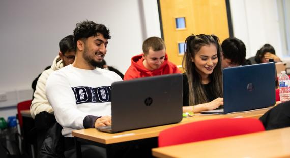 Male and female students in class and on laptops, laughing 