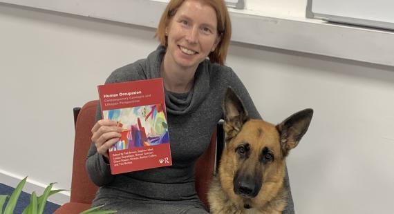 Dr Bethan Collins holding a book with Huntly, her guide dog